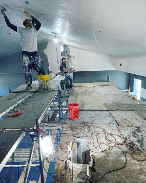 SUR crew veneer plastering a ceiling over blue board from scaffolding